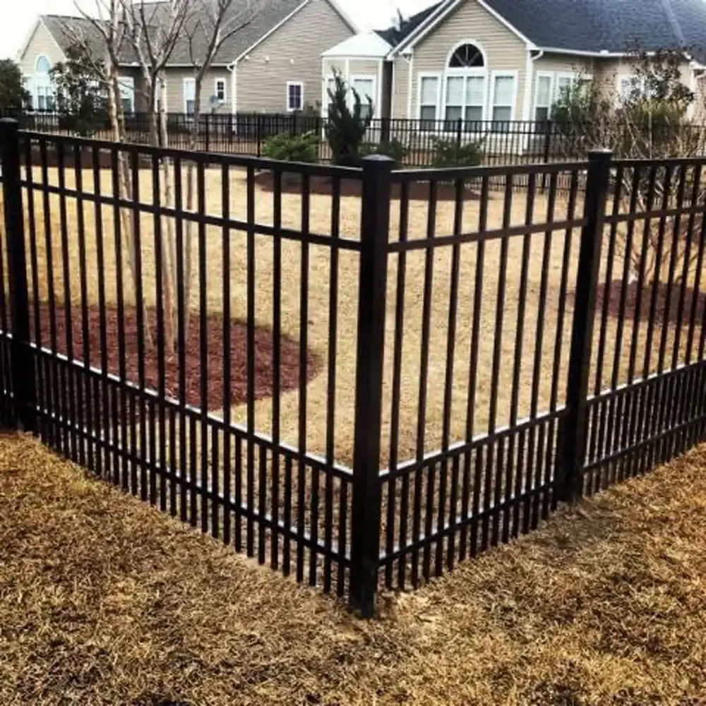 A black fence surrounds a lush green yard in front of a house