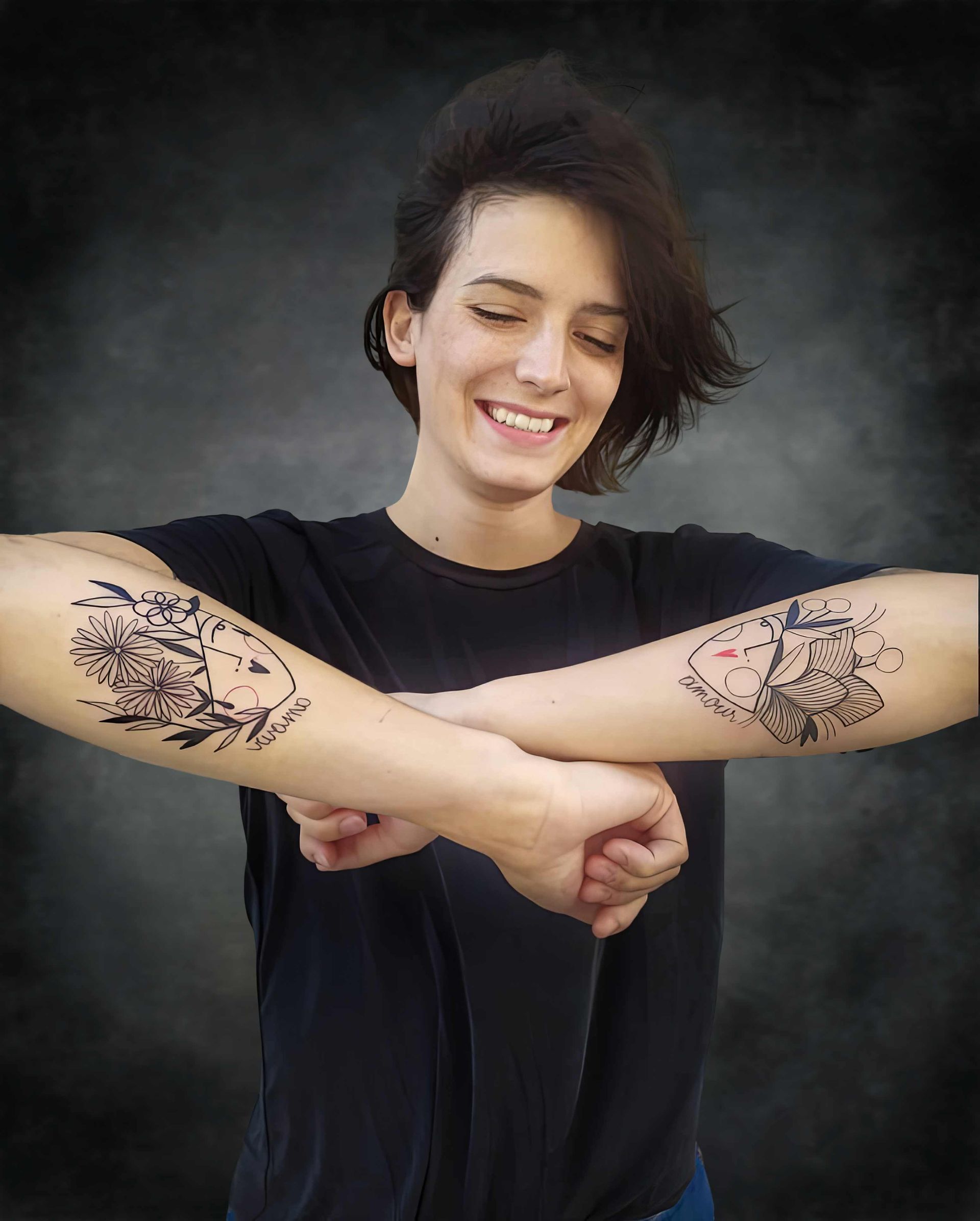 Une femme avec deux tatouages sur les bras sourit.