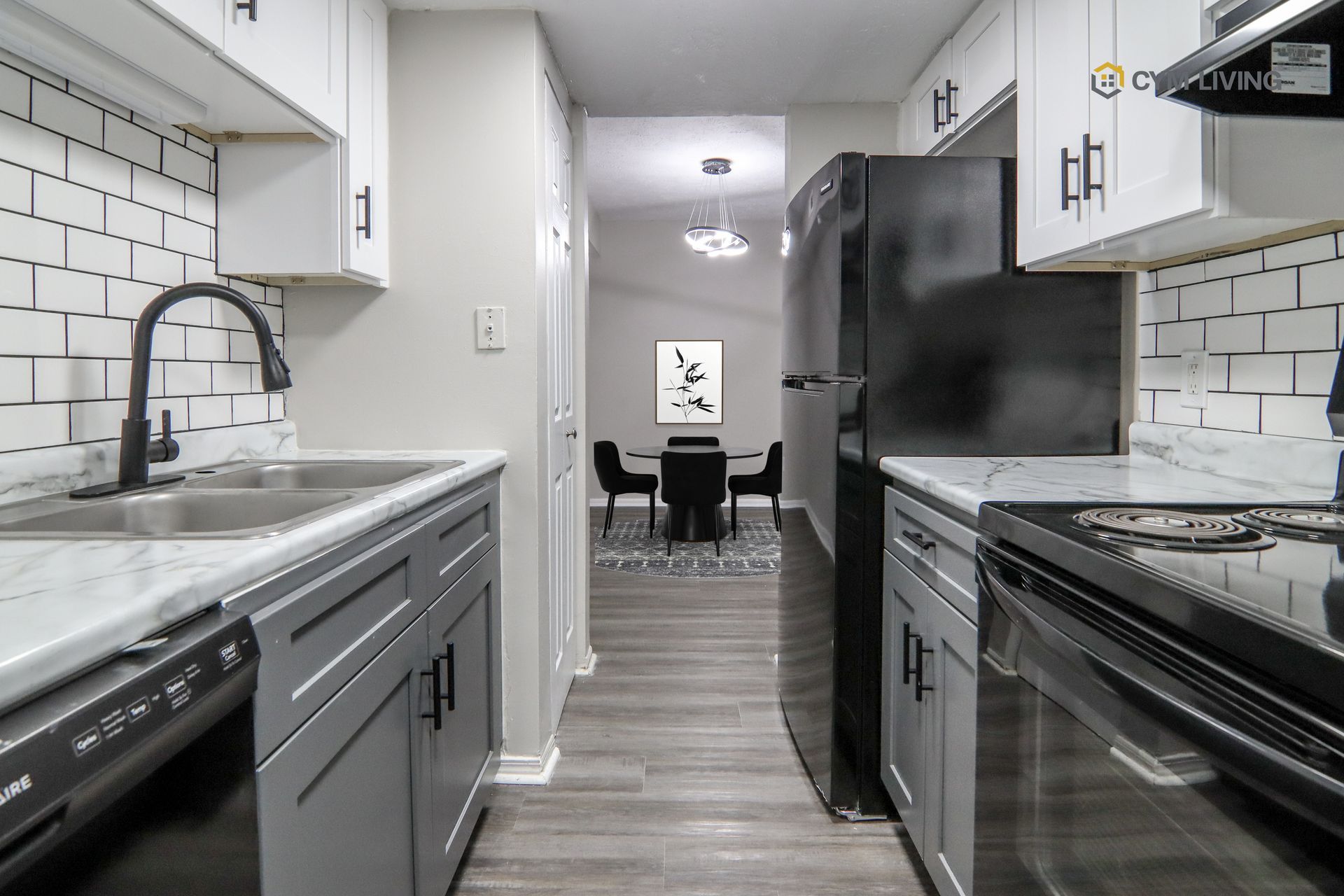 Kitchen with gray cabinets, white backsplash, black appliances, and dining area in the background.