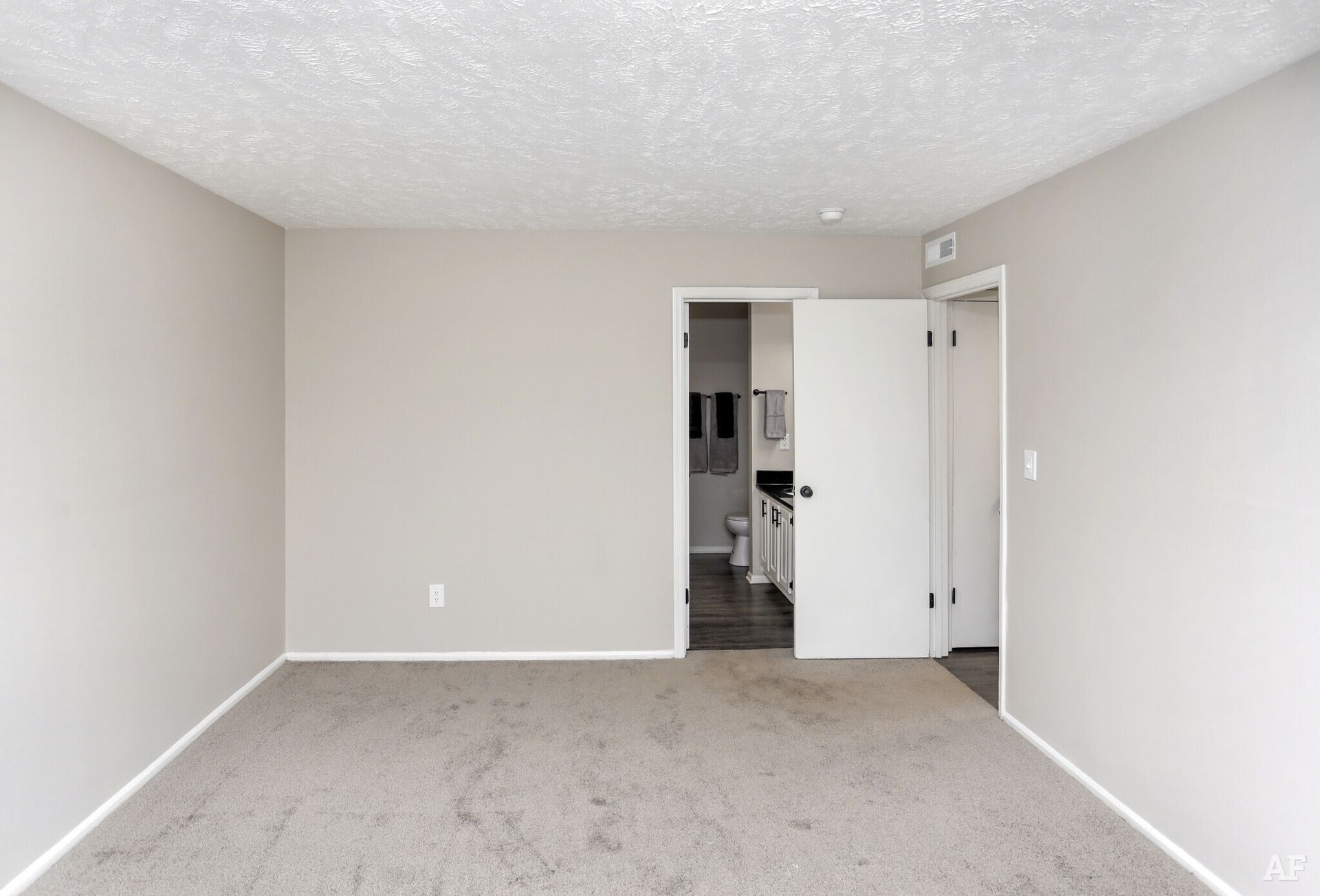 Empty room with gray walls, carpet, white ceiling, and doorway to a bathroom.