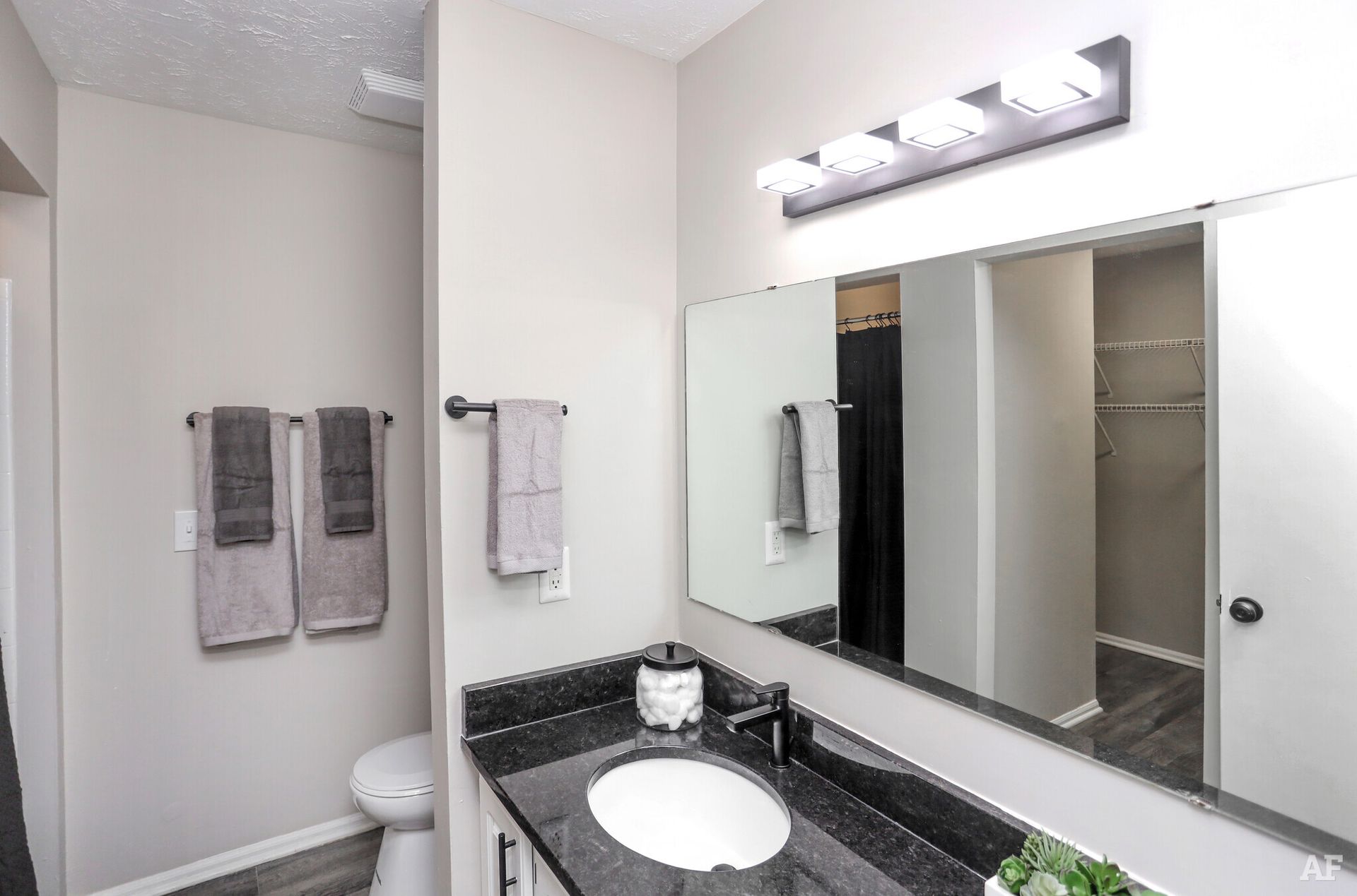 Bathroom with gray walls, black countertop, white sink, large mirror, and towel rack.