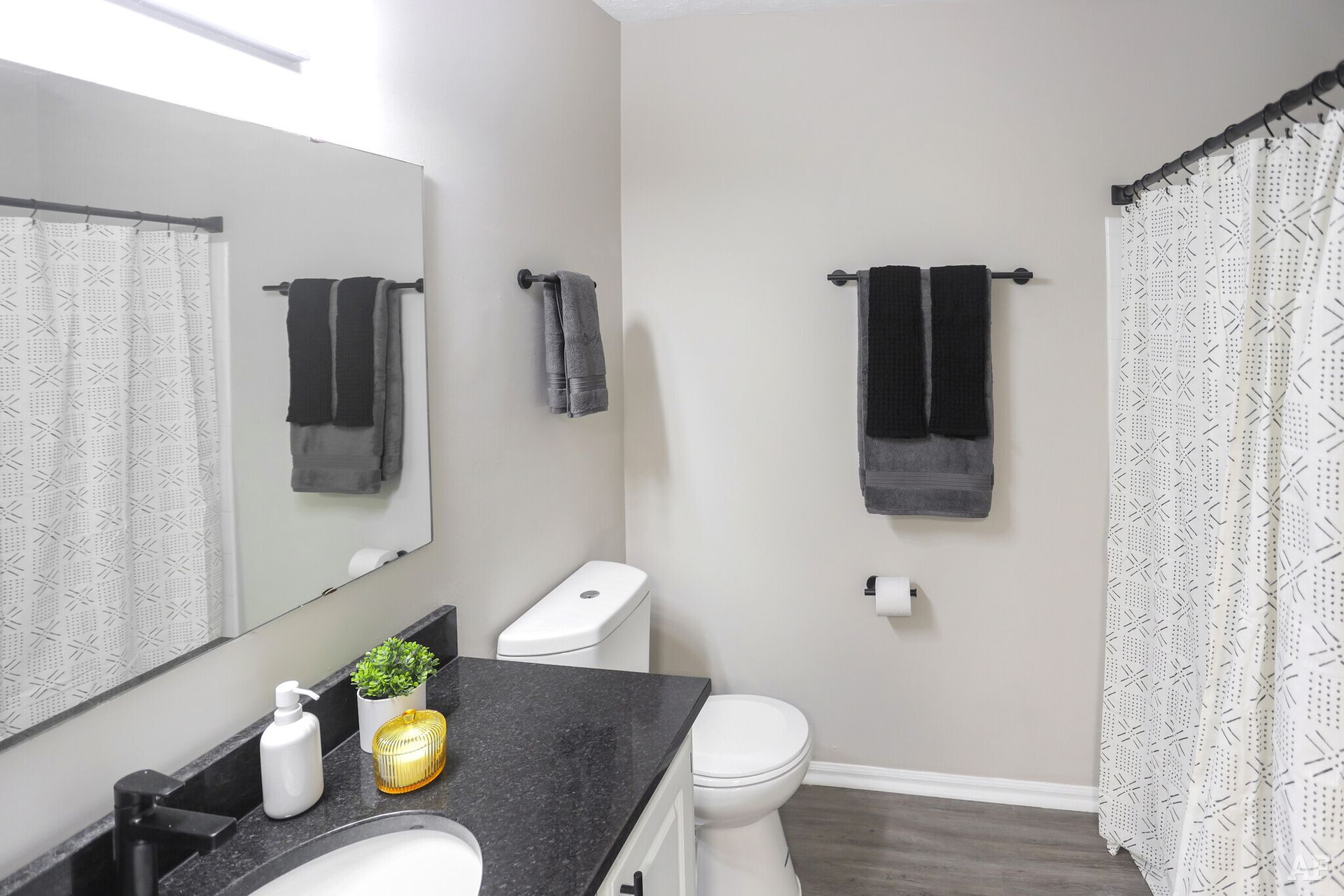 Bathroom with gray walls, white toilet, black countertop, and black towel rack with gray towels.