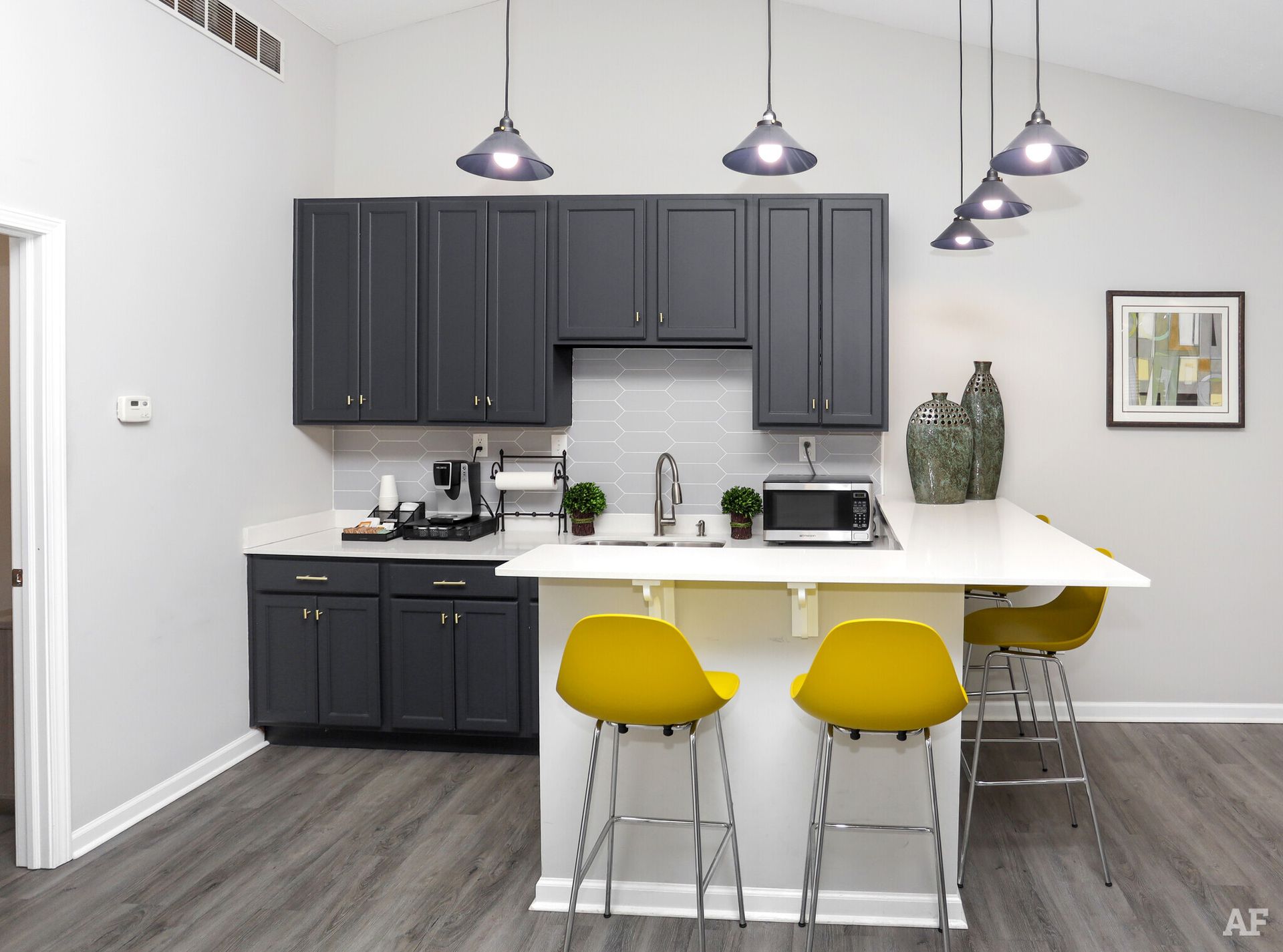 Kitchen with dark gray cabinets, white countertop island, yellow chairs, and gray flooring.