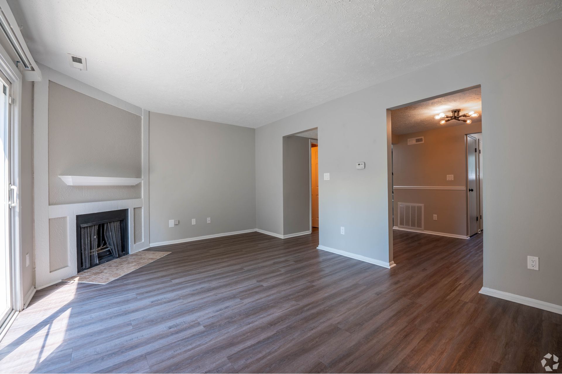Empty living room with fireplace and dark wood-look flooring. Gray walls, natural light from the sliding door.