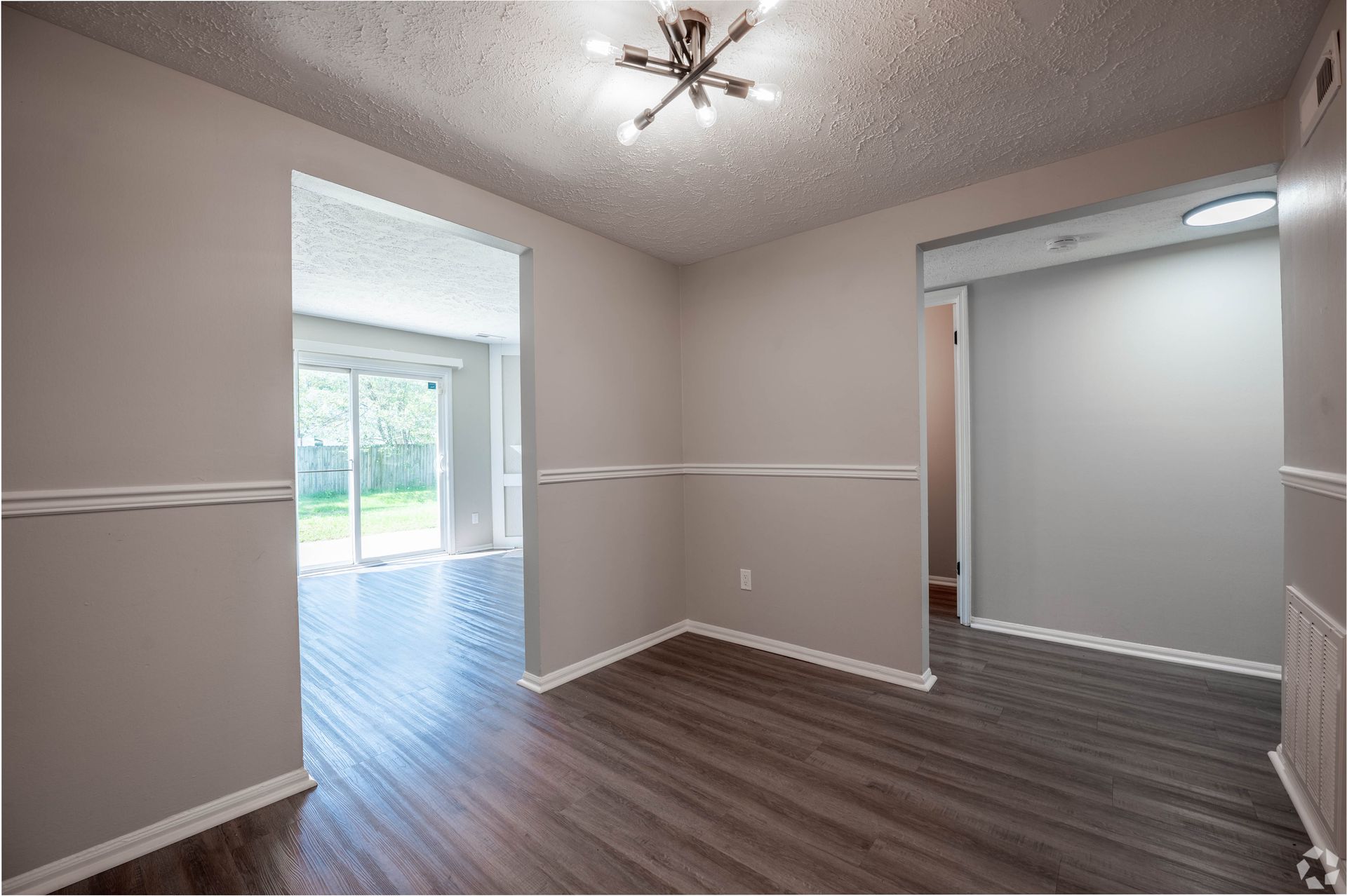 Empty dining area with dark wood-look flooring, neutral walls, and an open doorway to a backyard.