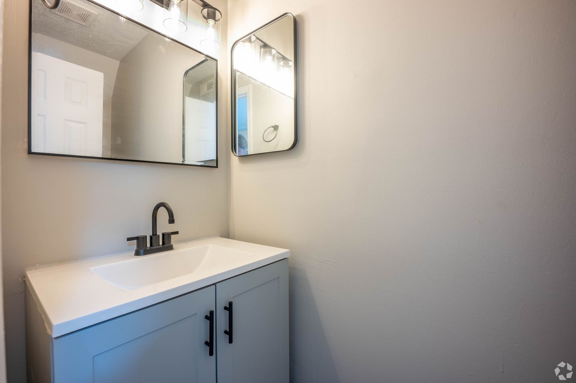 Small bathroom with a blue vanity, white countertop, and two mirrors.