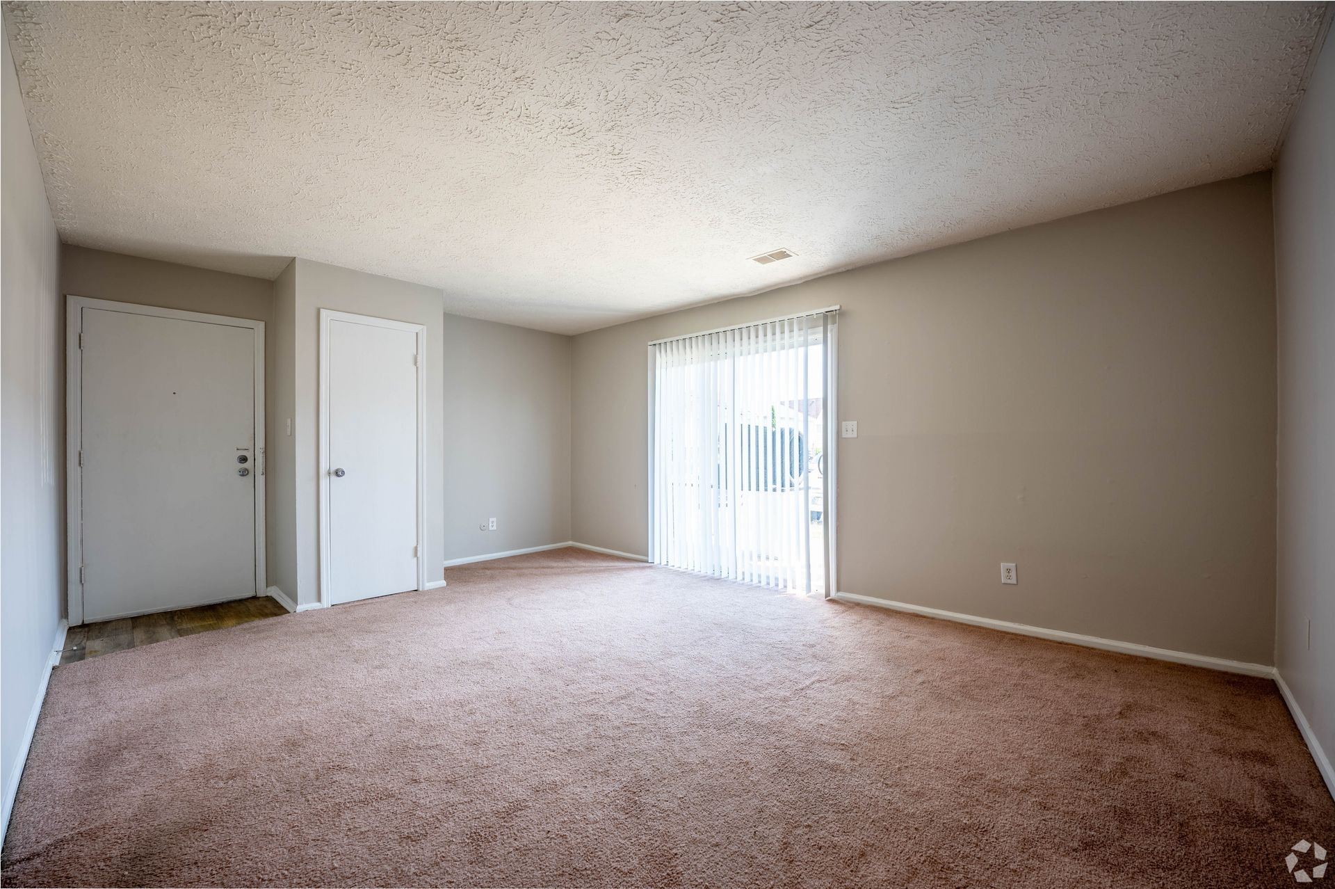 Empty room with brown carpet, tan walls, and sliding glass door.