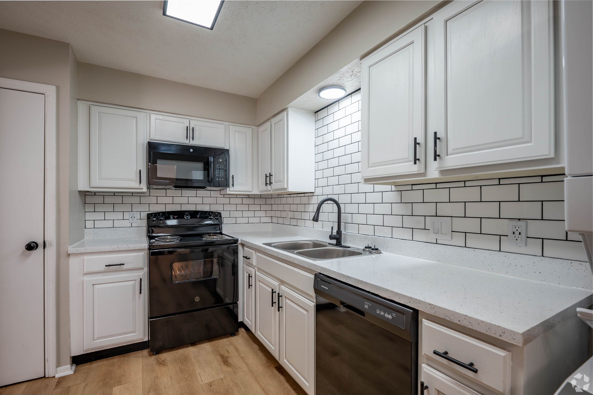 White kitchen with black appliances, subway tile backsplash, and wood-look flooring.