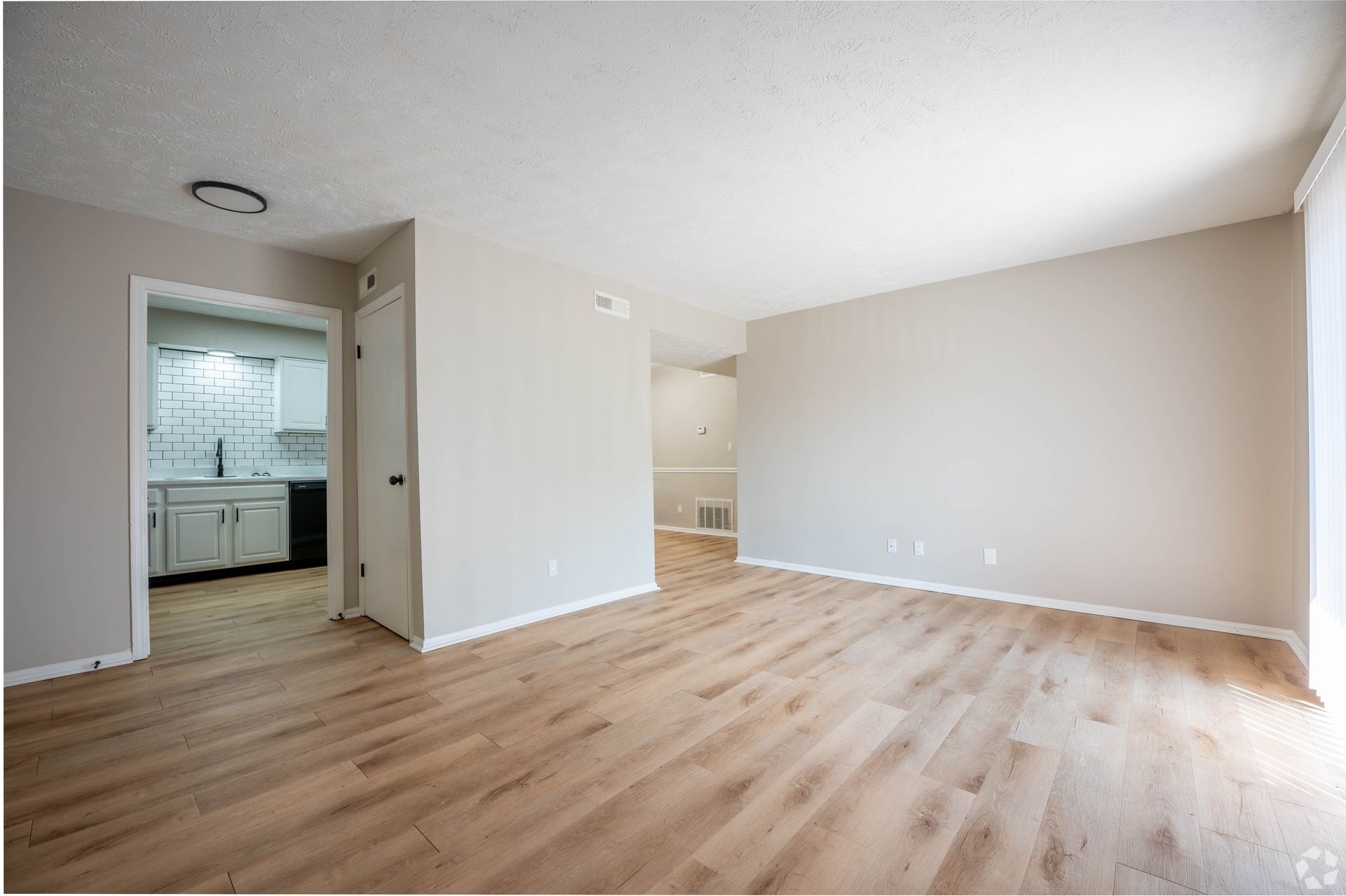 Empty living room with wood flooring, neutral walls, and view of kitchen doorway.