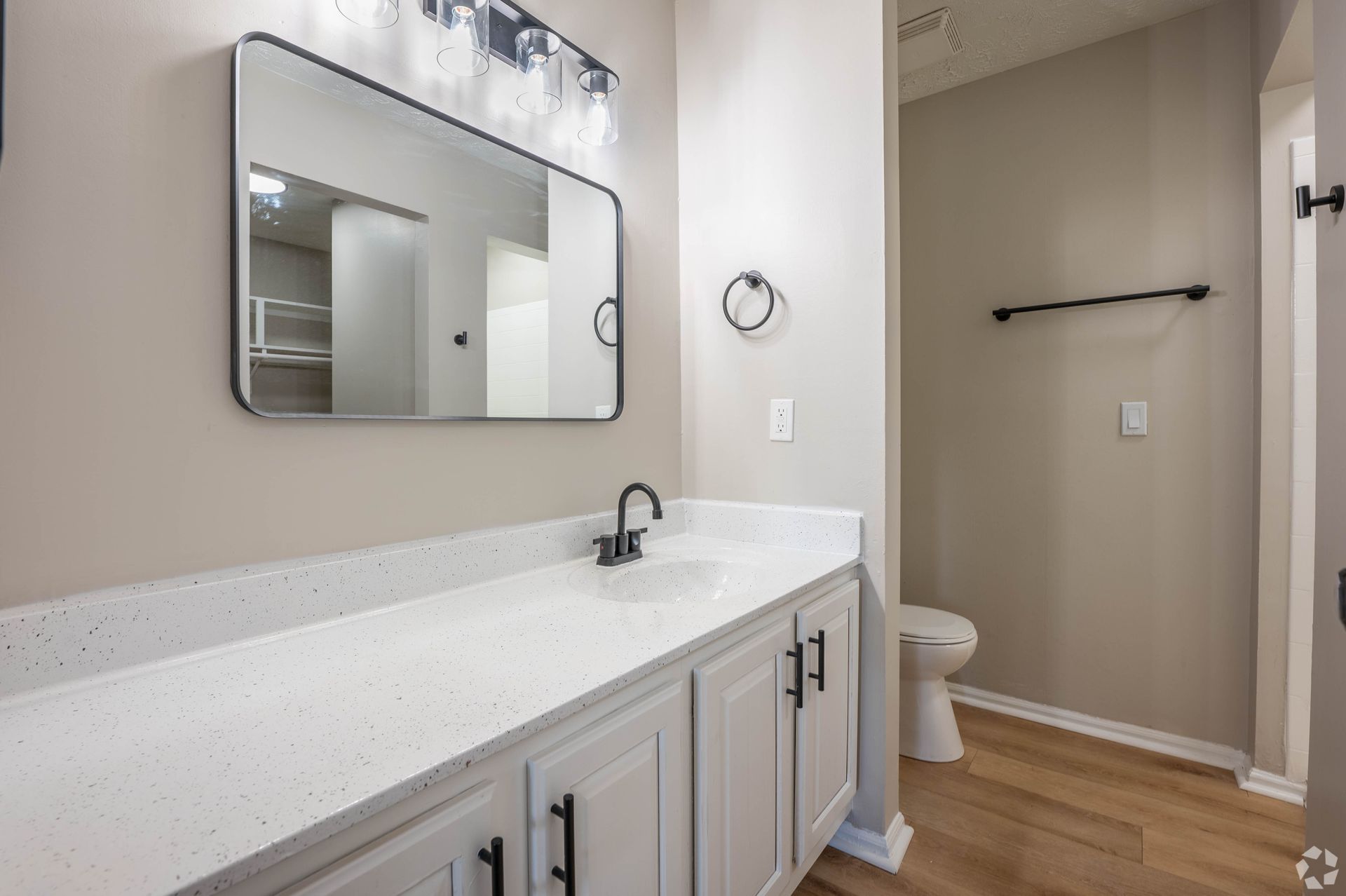 Bathroom with white countertop, light gray cabinets, black faucet, mirror, and toilet.
