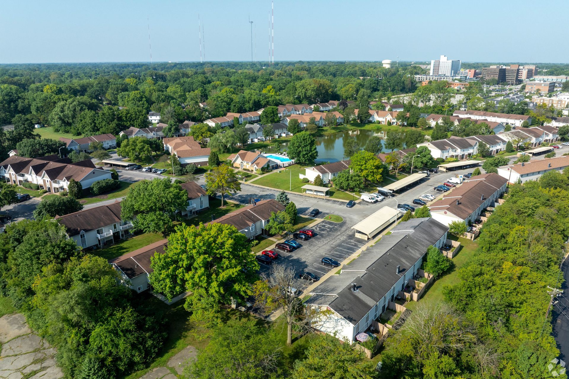 Aerial view of suburban houses and a small pond, green trees, and a city skyline.