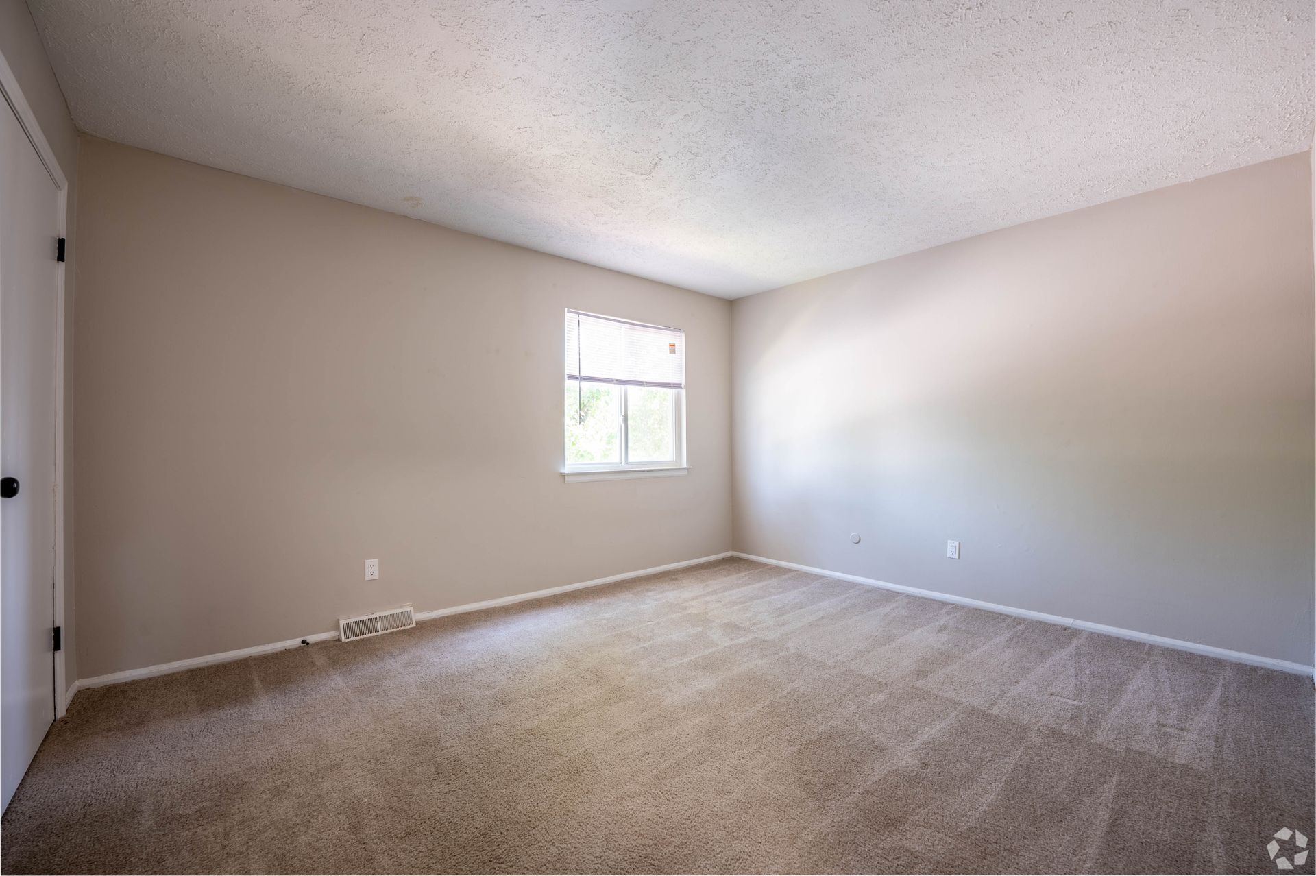Empty bedroom with beige walls and carpet; small window, white trim.