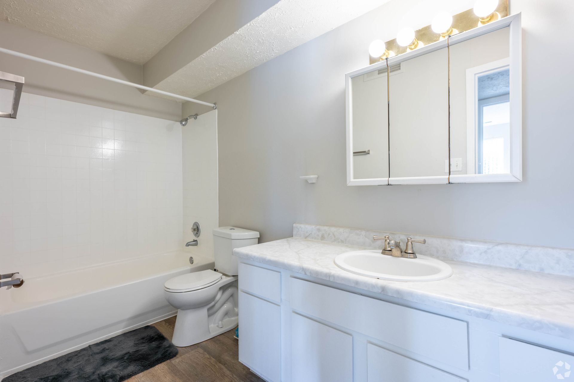 Bathroom with white tub, toilet, and vanity with a sink. Gray walls and light fixtures.