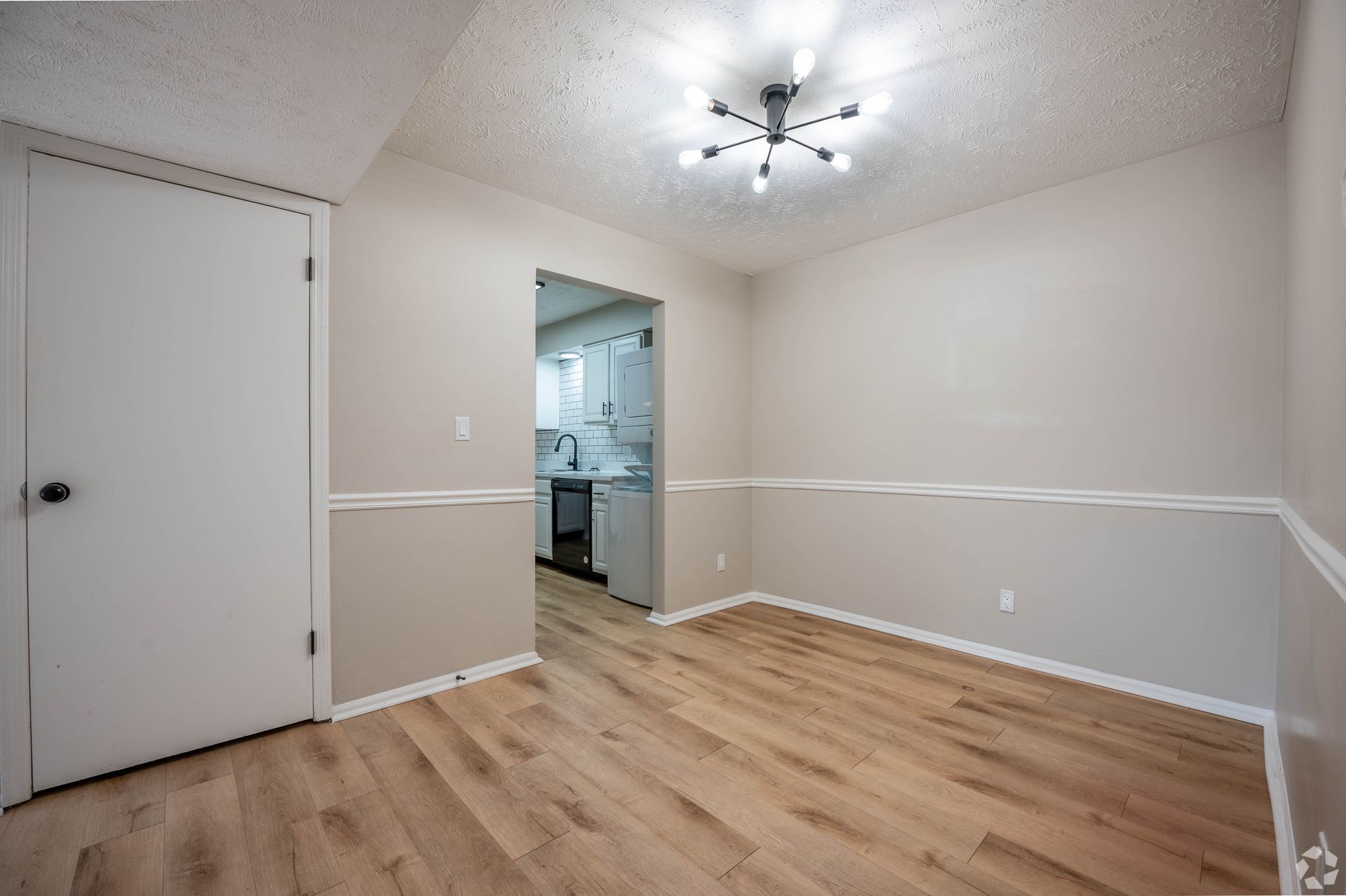 Empty dining room with light wood floors, neutral walls, and a view to the kitchen.