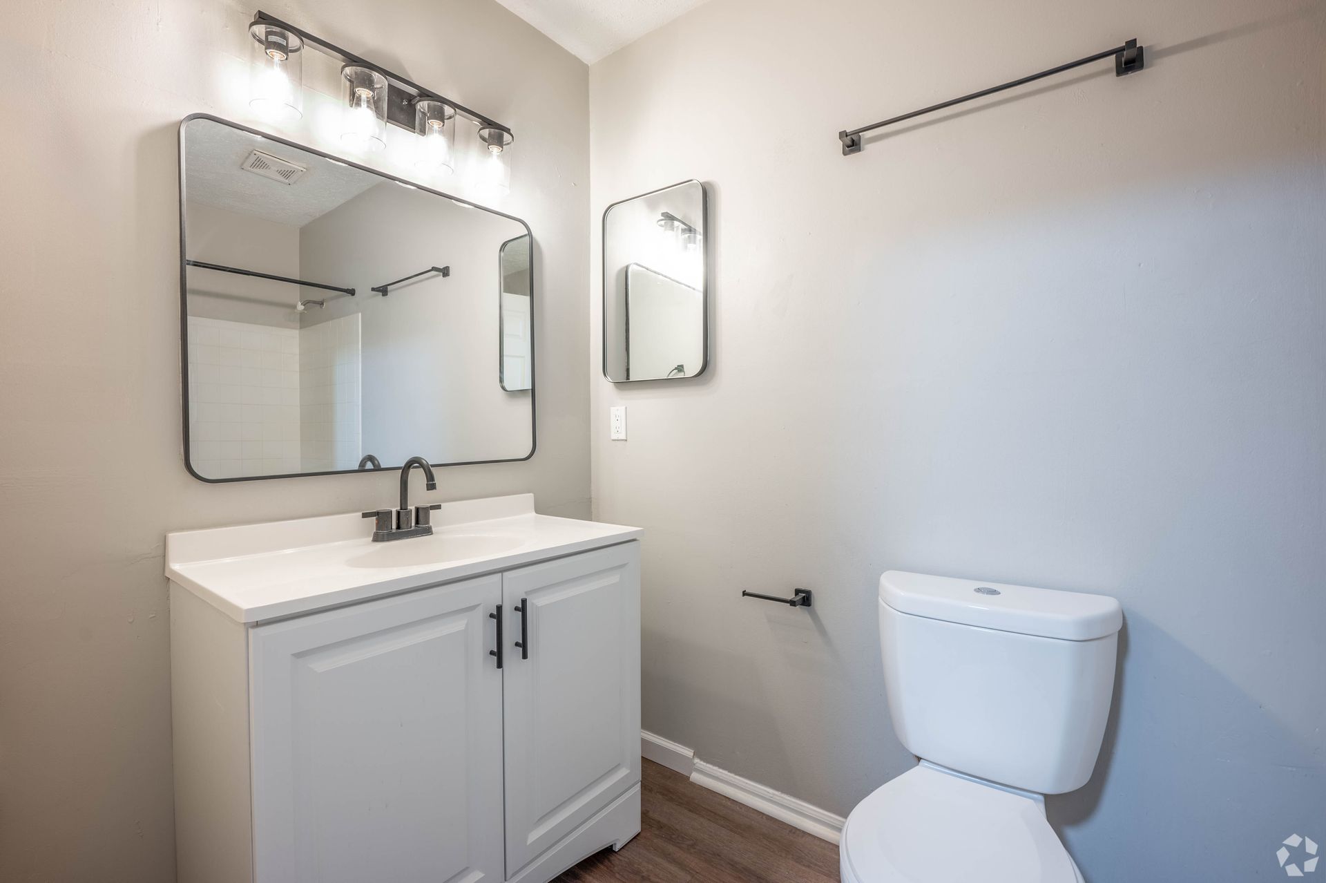 Bathroom with white vanity, toilet, and mirrors on gray walls.