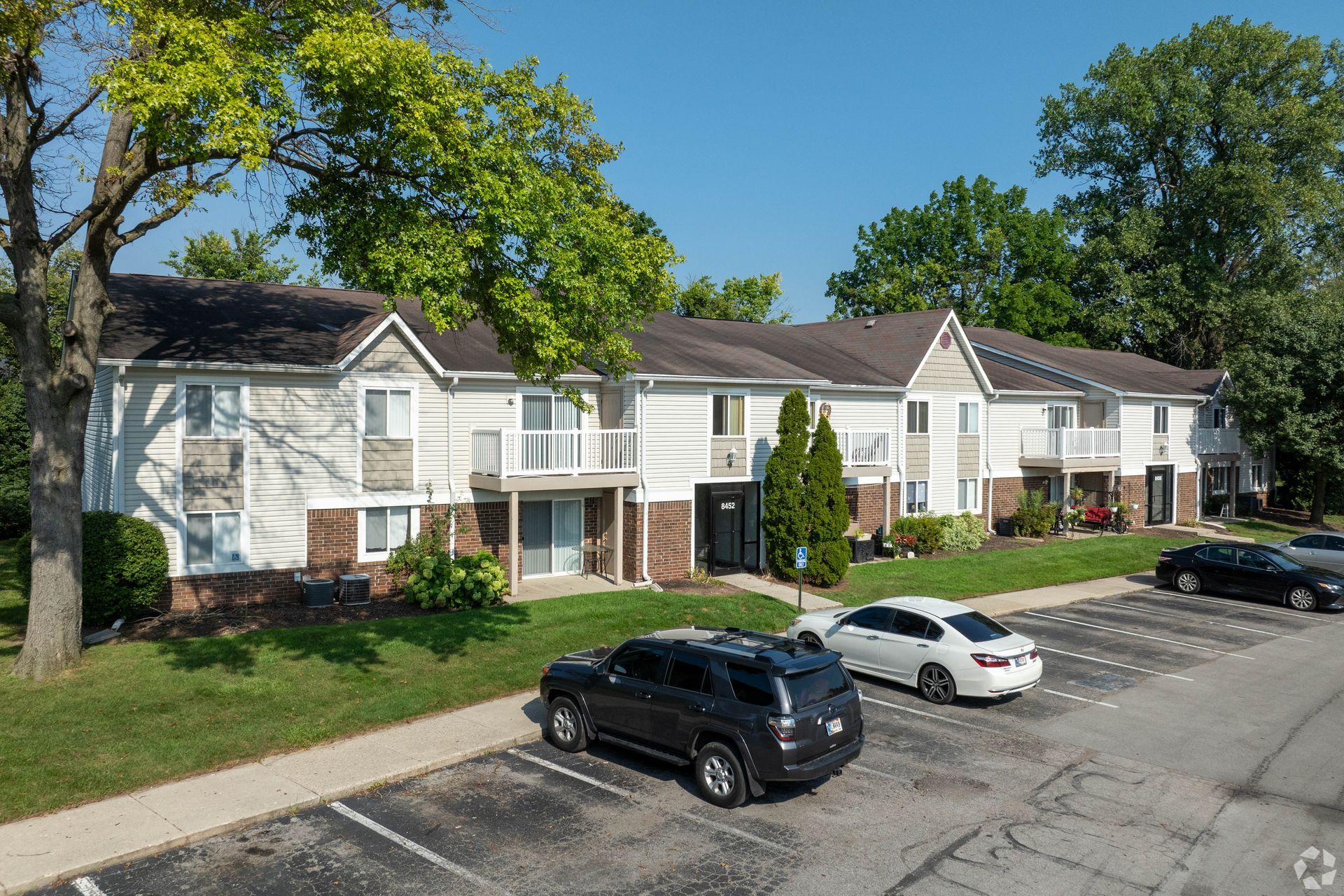 Apartment complex with cars parked in a lot; exterior shot on a sunny day.