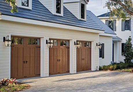 Three-car garage with brown doors on a white house. Black lamps flank each door.
