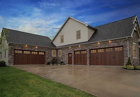 Multi-car garage with brown doors, stone facade, and a dark shingle roof, under a blue sky.
