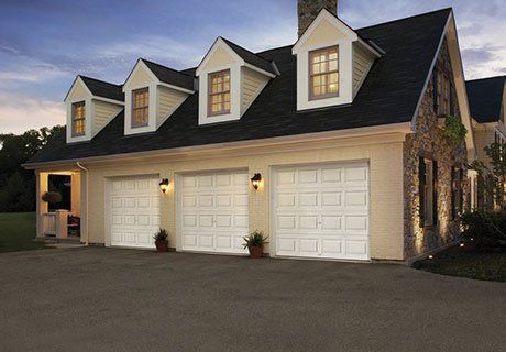 Three-car garage with white doors, dormers, and stone accents on a house at dusk.
