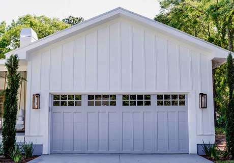 White barn-style garage with gray door and windowed top panel. Two sconces flank the door.