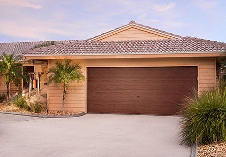 Beige house with brown garage door, palm trees, and concrete driveway.