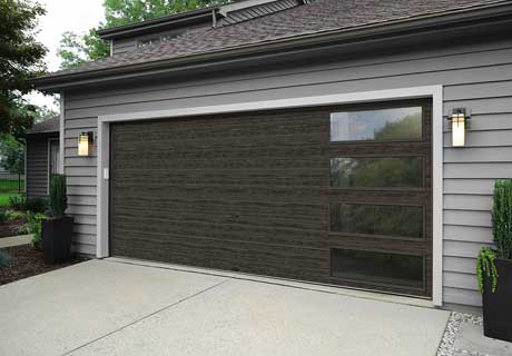 Modern gray garage door with windows; mounted on a gray-sided house.