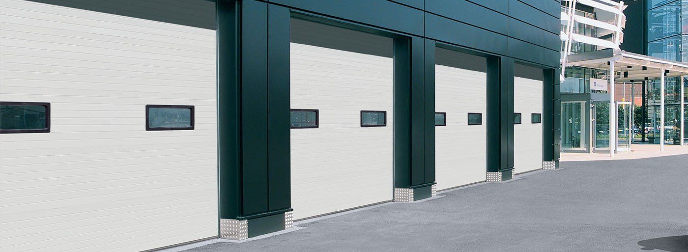 Exterior of a building with a row of white garage doors. Each door has a small, rectangular window.