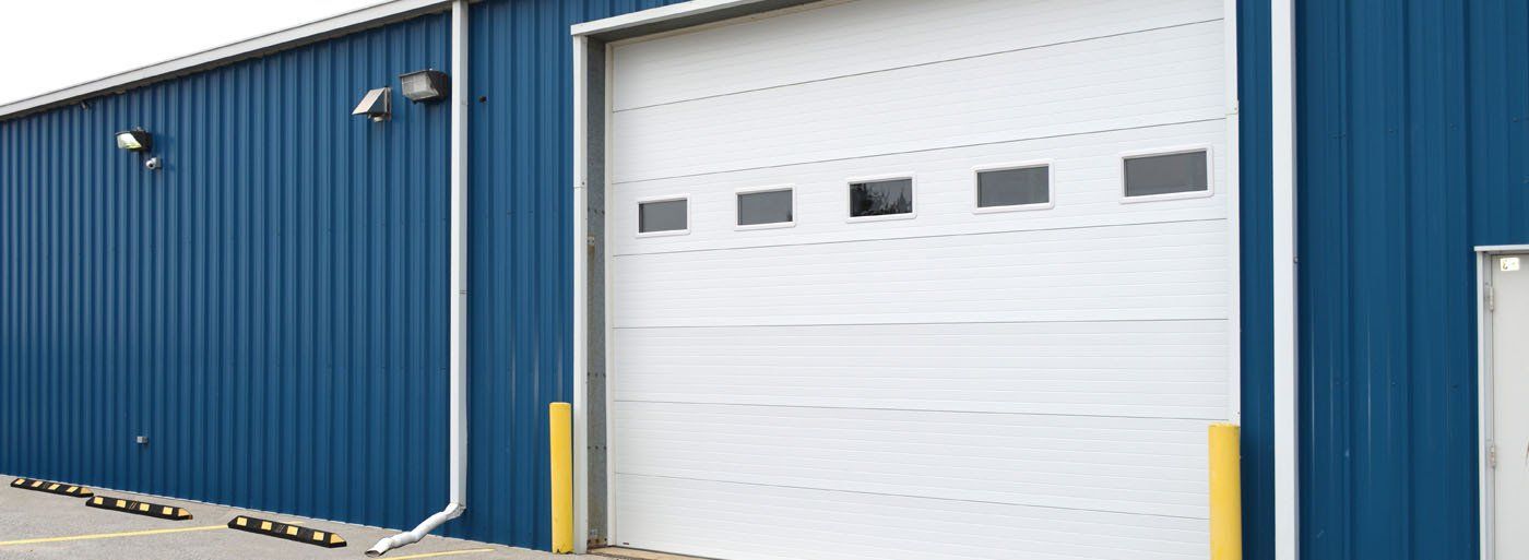 Blue industrial building with a white garage door and yellow bollards.
