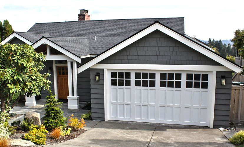 Gray house with white trim, white garage door, and a brown door. Landscaping in front.