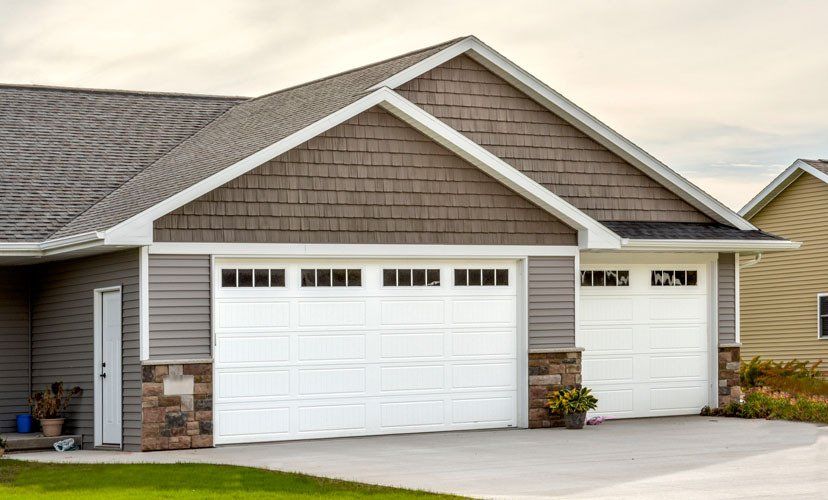 Two-car garage with white doors, gray siding, and brown roof. Stone accents and concrete driveway.