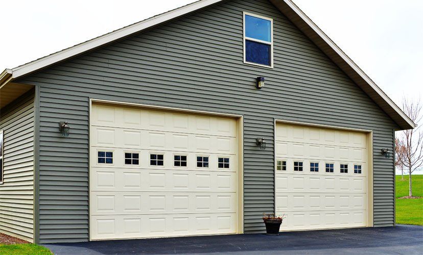 Two-car garage with tan doors, green siding, and small windows.