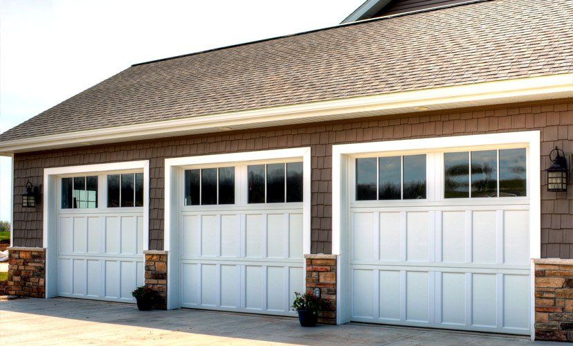 Three white garage doors with windows, brown siding, and stone accents under a brown roof.