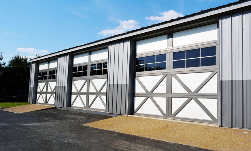 Three gray and white garage doors with windows, in a gray metal building, on a sunny day.