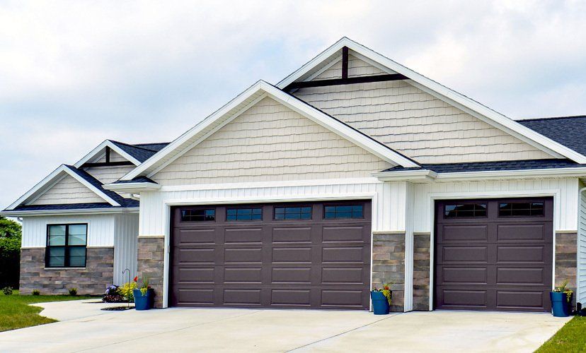 A house with two brown garage doors, beige siding, and stone accents against a cloudy sky.