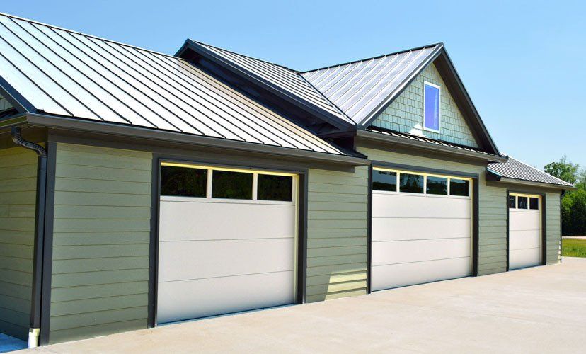Three-car garage with white doors, green siding, and metal roof under a blue sky.