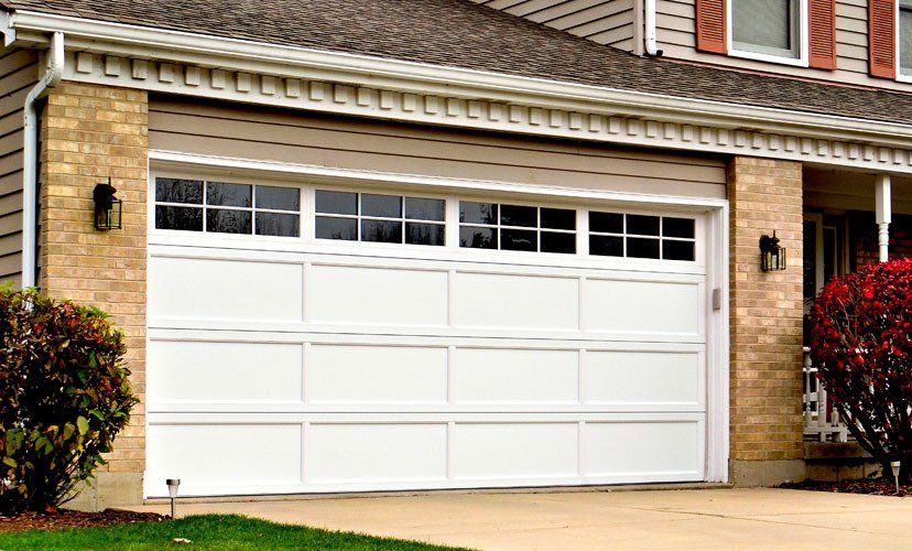 Installation White garage door with windows, set in a brick and beige home.