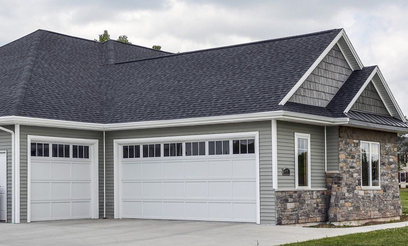 Garage with two white doors, gray siding, stone accents, and a dark roof.