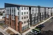 Exterior view of a modern apartment building with a parking lot in front.