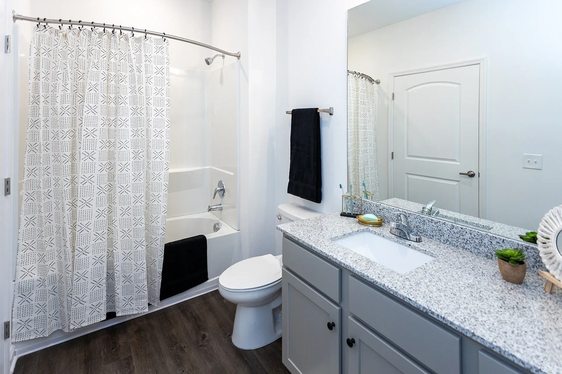 Modern bathroom with a granite countertop vanity, white sink, and a bathtub with a shower.