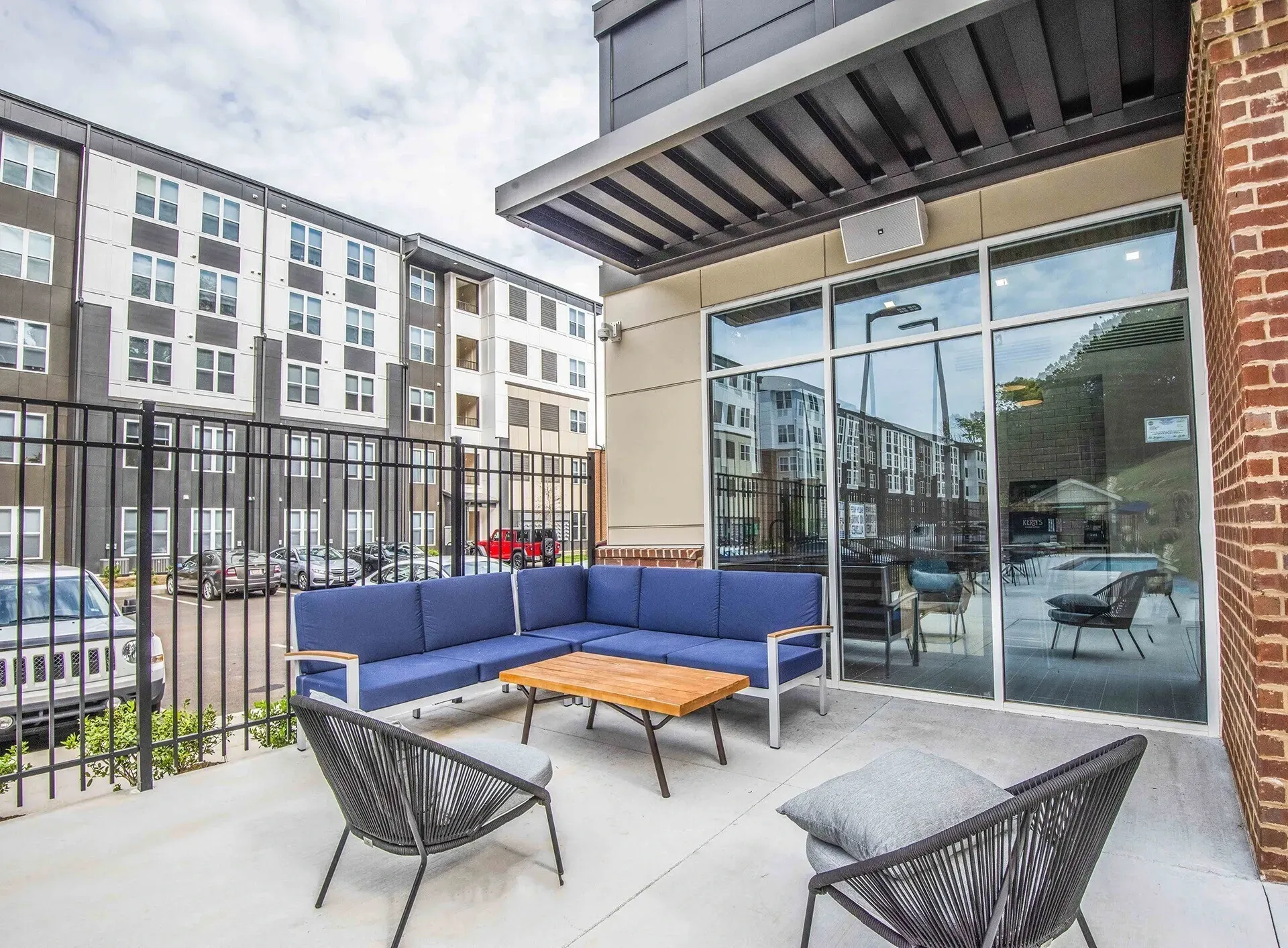 Outdoor seating area with blue sectional couch and coffee table on a patio, with apartment buildings in the background.