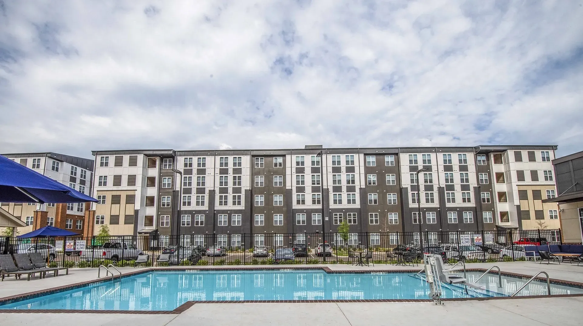 Exterior view of a modern apartment building with a swimming pool in the foreground.