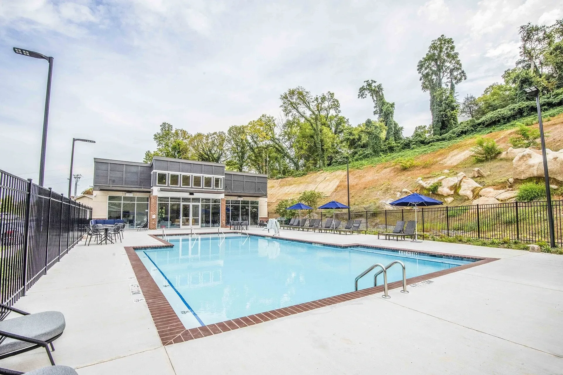 Outdoor swimming pool area with lounge chairs and umbrellas, adjacent to a modern building.