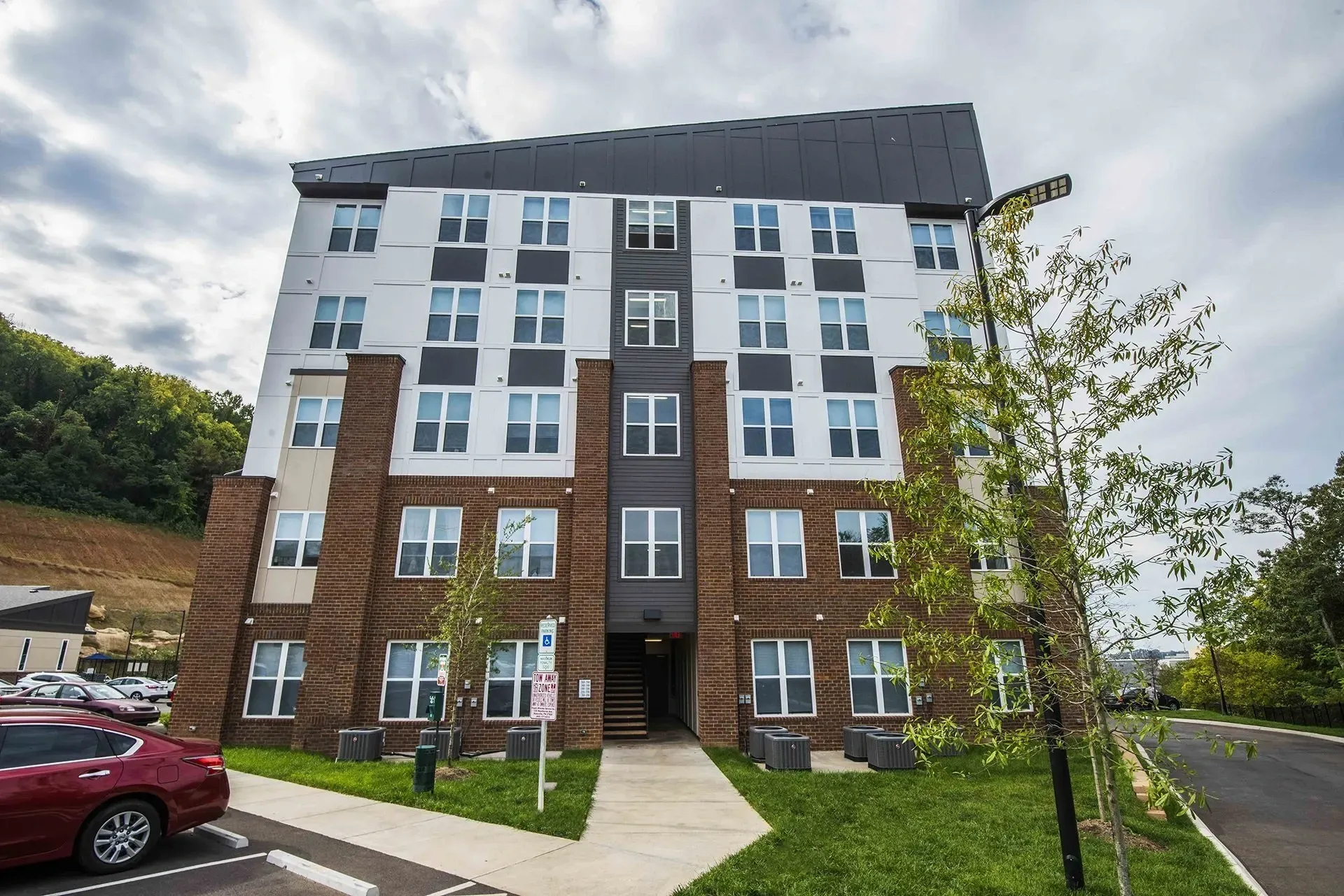 Exterior of a modern apartment building with brick and white siding, featuring large windows and a sloped roof.