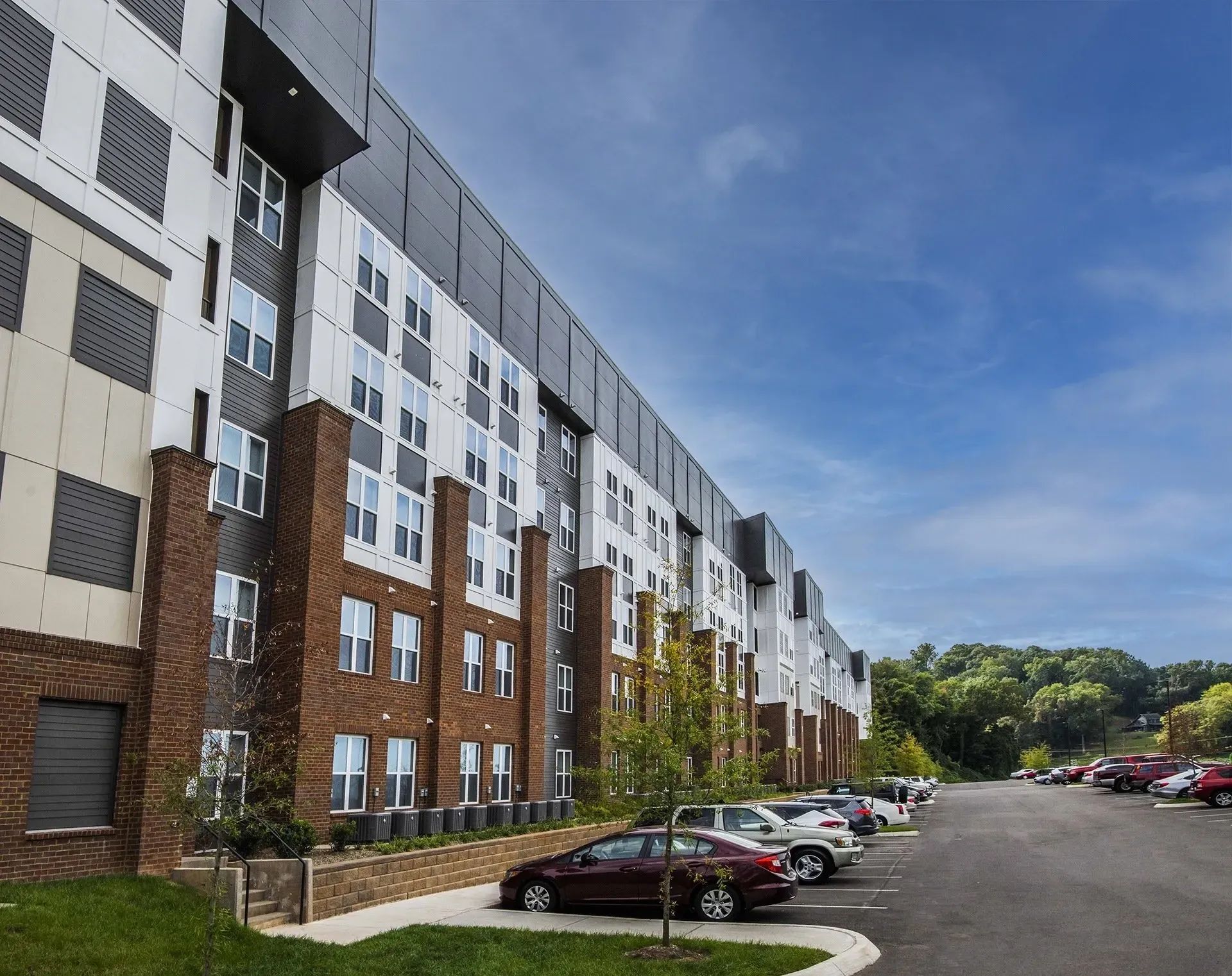 Modern apartment building exterior with brick and metal facade and a parking lot.