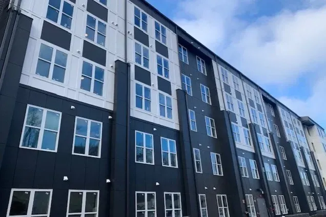 Exterior of a modern apartment building with dark and white siding and many windows.