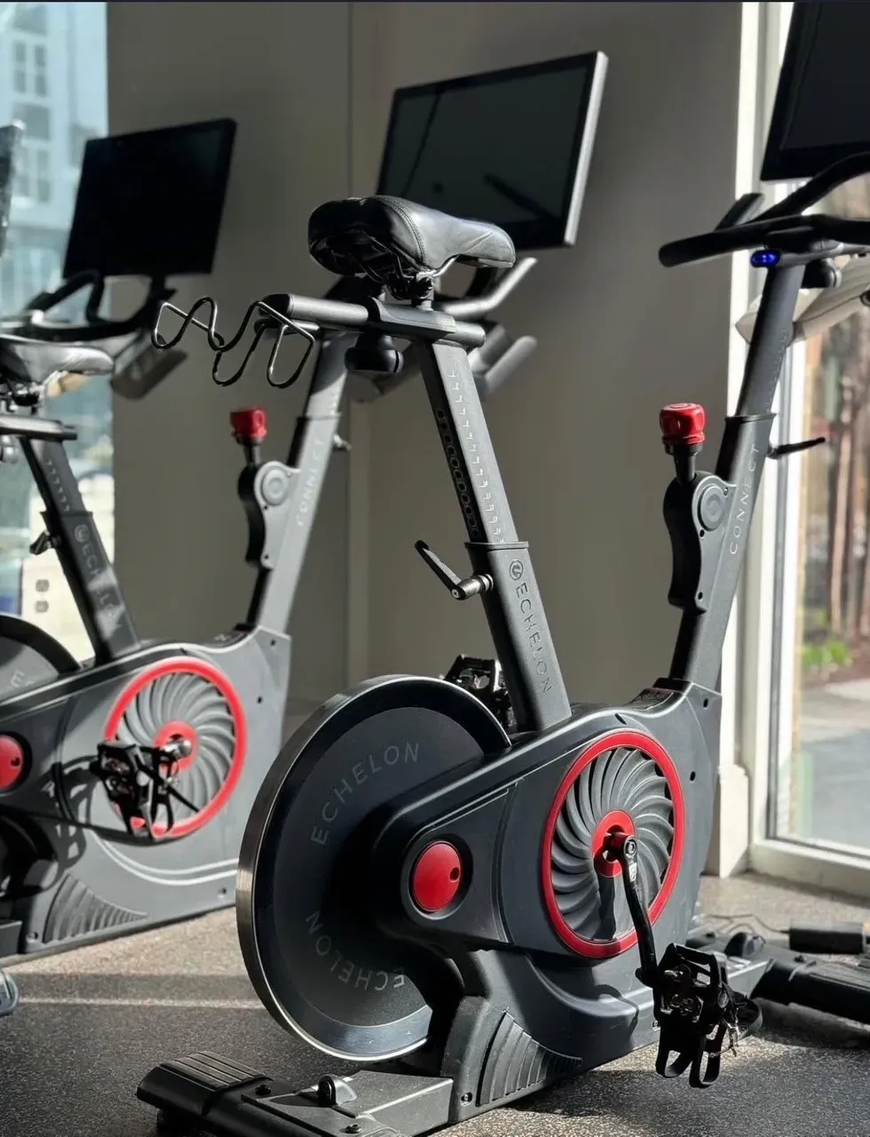 Two Echelon stationary bikes with screens in a gym.