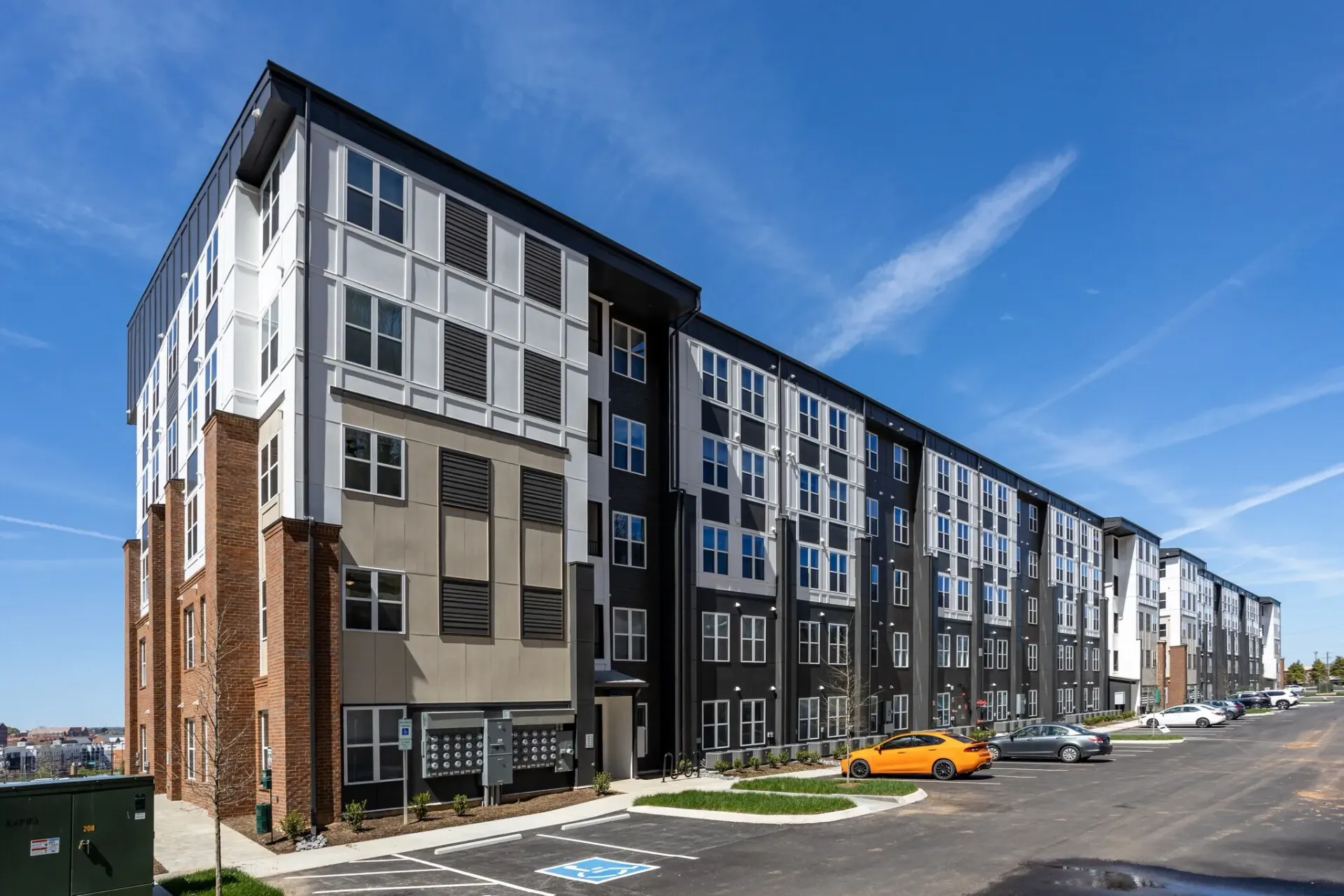 Exterior view of a modern apartment building with a black and white facade, large windows, and brick accents, under a blue sky with clouds.
