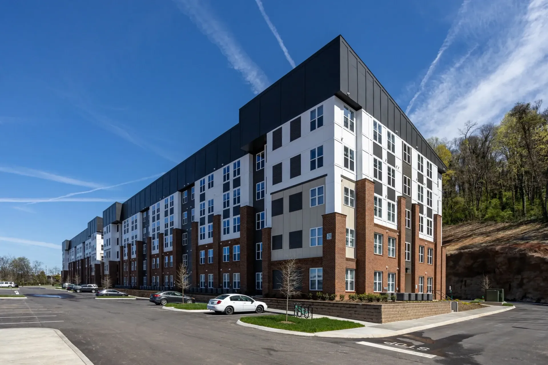 Modern apartment building exterior with brick and white siding, parked cars, and a clear blue sky.