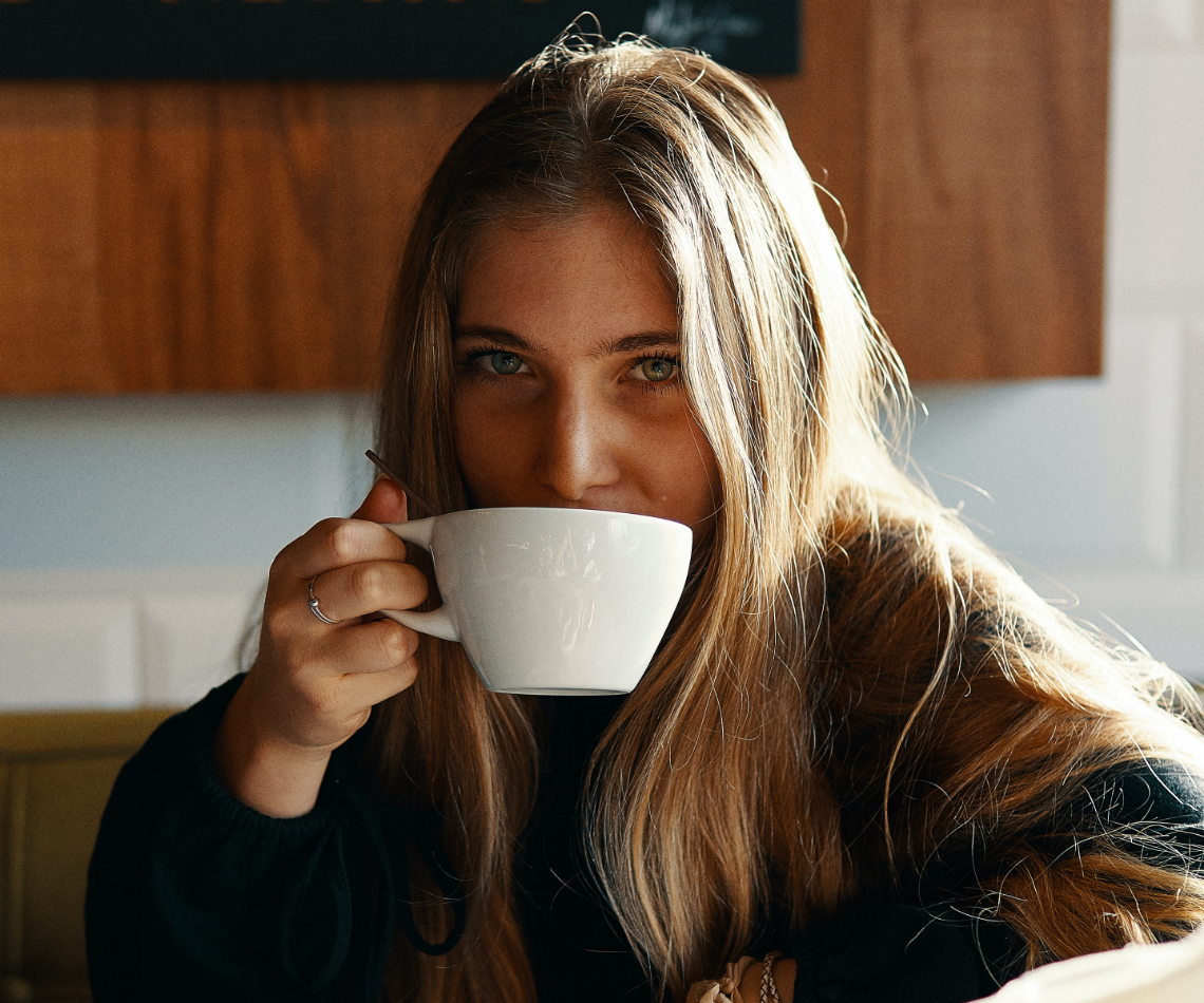 A woman with long hair is drinking a cup of coffee.