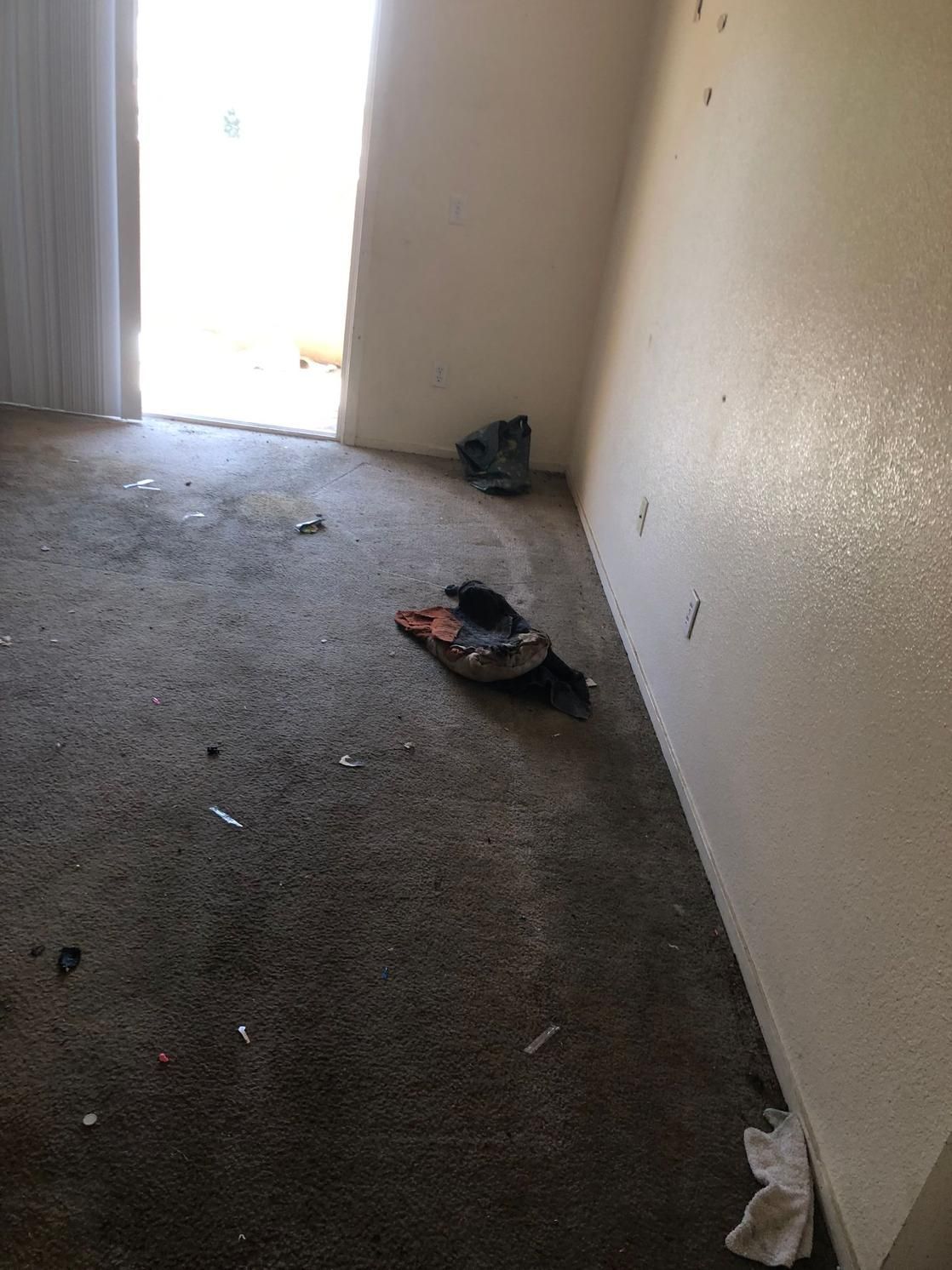 Dim empty room with a bright doorway and scattered debris on the concrete floor.